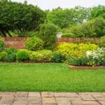 Backyard English Cottage Garden On Brown Pavement And Green Lawn